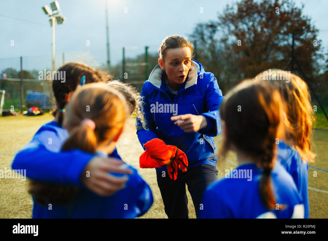 Girls soccer team listening to coach on field at night Stock Photo