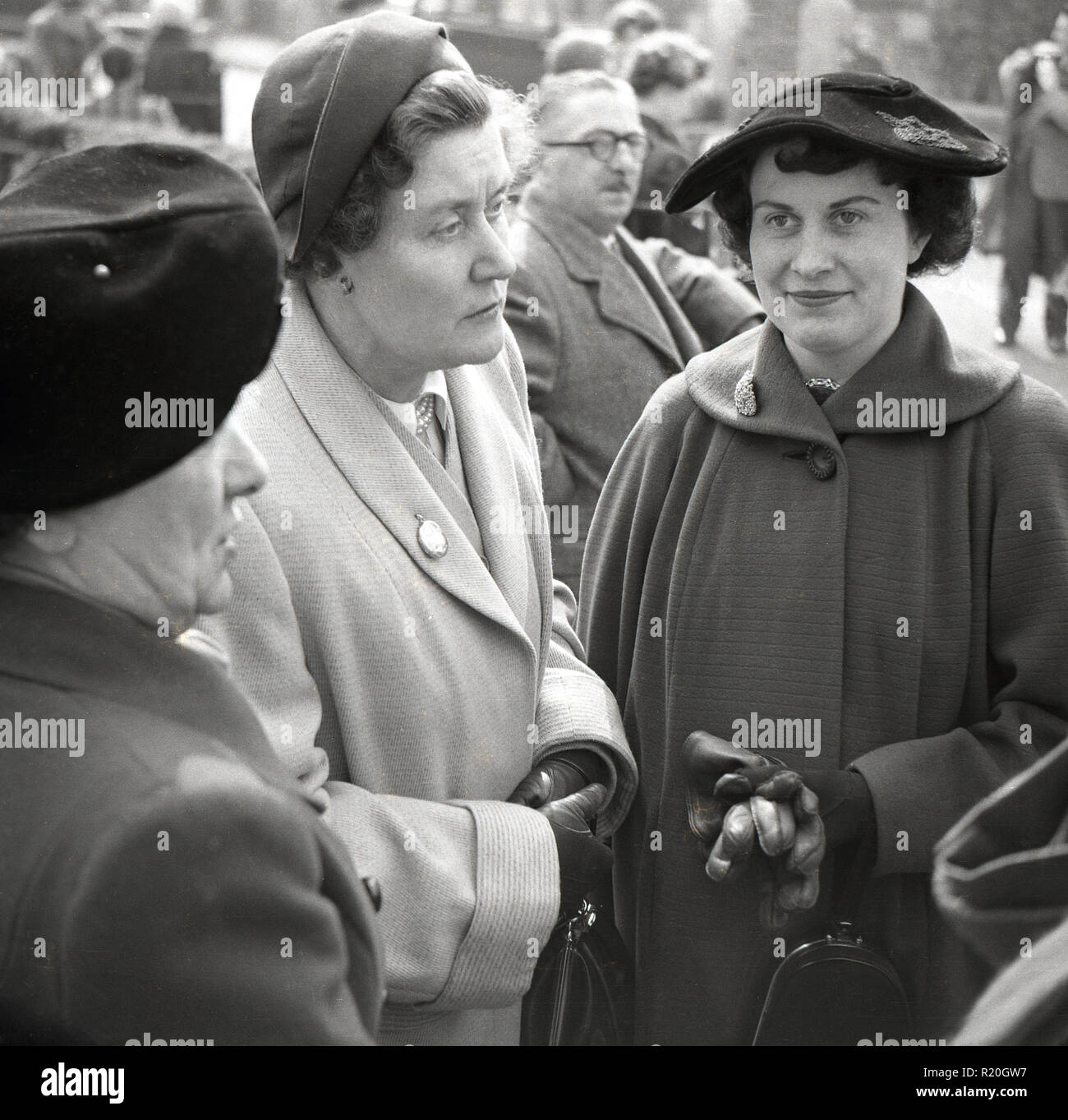 1950s, three ladies dressed in coats and hats standing together outside ...