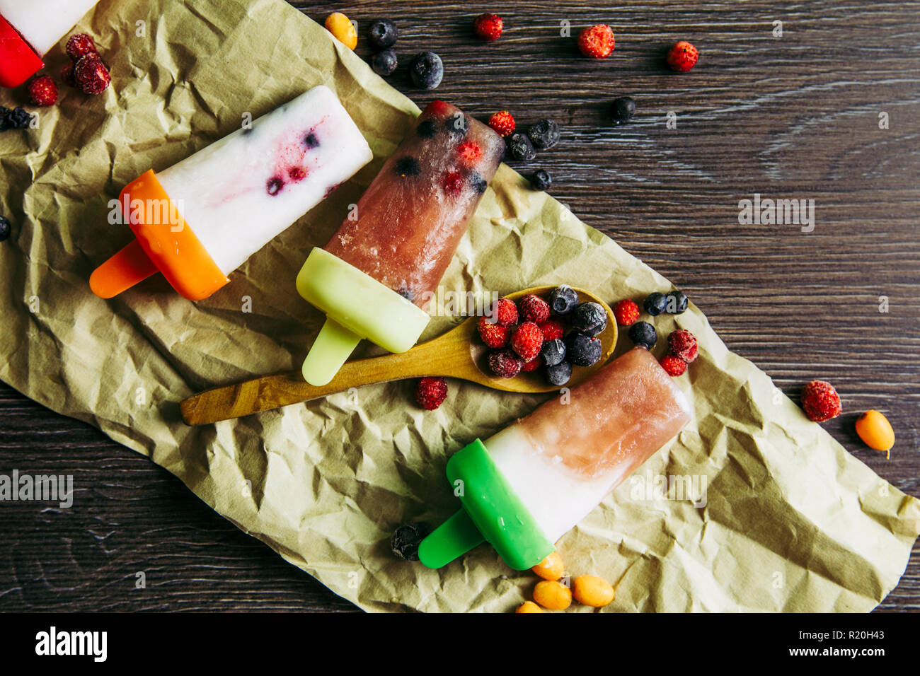 Flat lay view of lot of home made fridge frozen smoothie yogurt juice ice creams with wild berries on dark dramatic wooden background. Healthy snack c Stock Photo