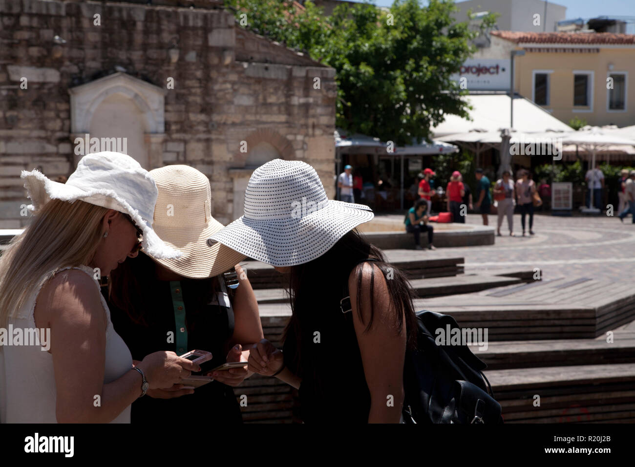 three young women with white sun hats looking at mobile phones plateia monastiraki athens greece Stock Photo