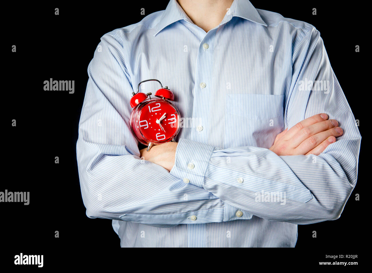 Adult male wearing formal shirt and hands crossed holding big red vintage alarm clock. Time concept. Stock Photo