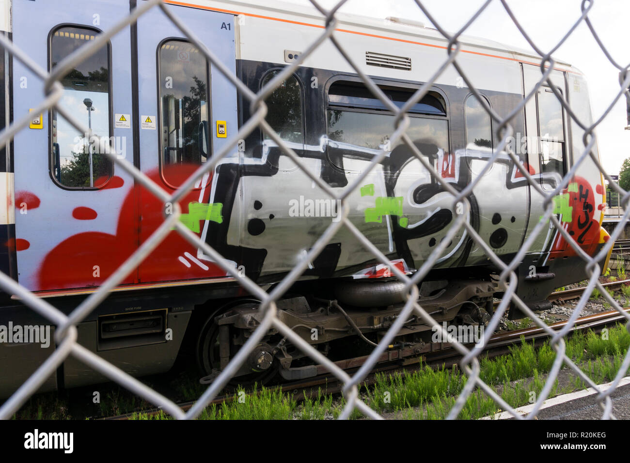 Train covered in graffiti seen through chain link fence. Stock Photo