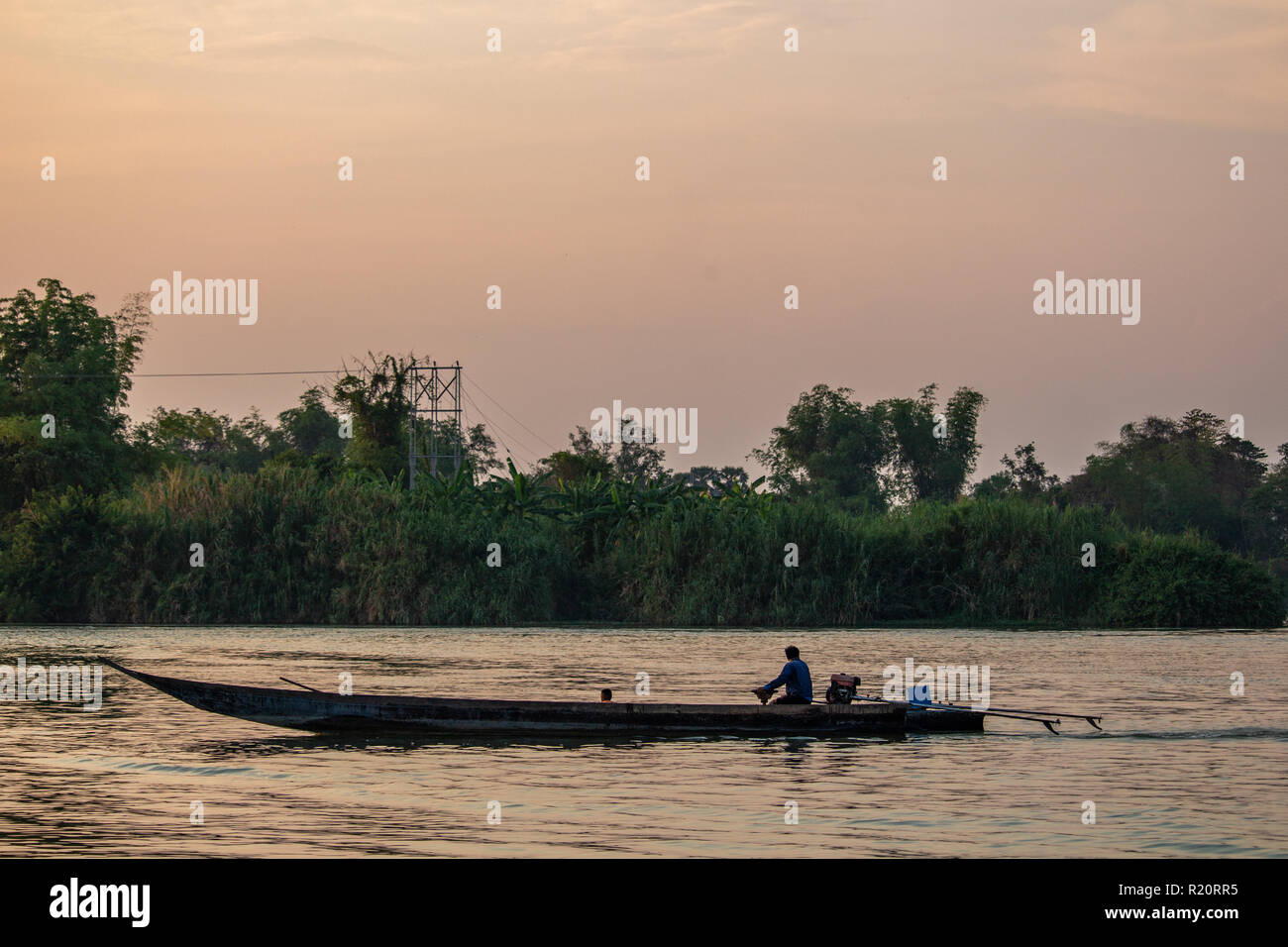 Don Det, Laos - April 22, 2018: Boat crossing the Mekong river surrounded by a green landscape at dusk Stock Photo