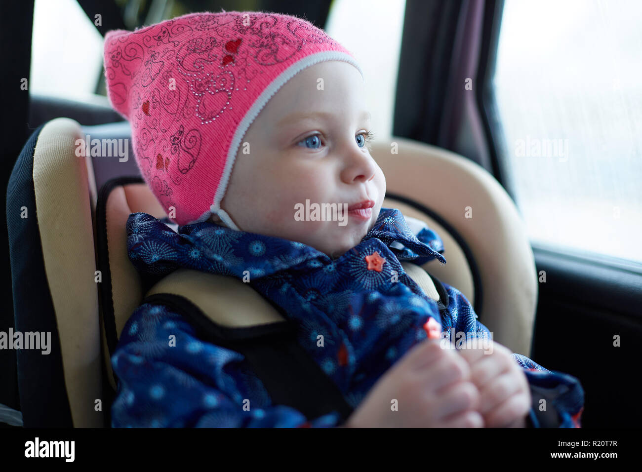 little girl with blue eyes sitting in a child seat in the back seat of ...