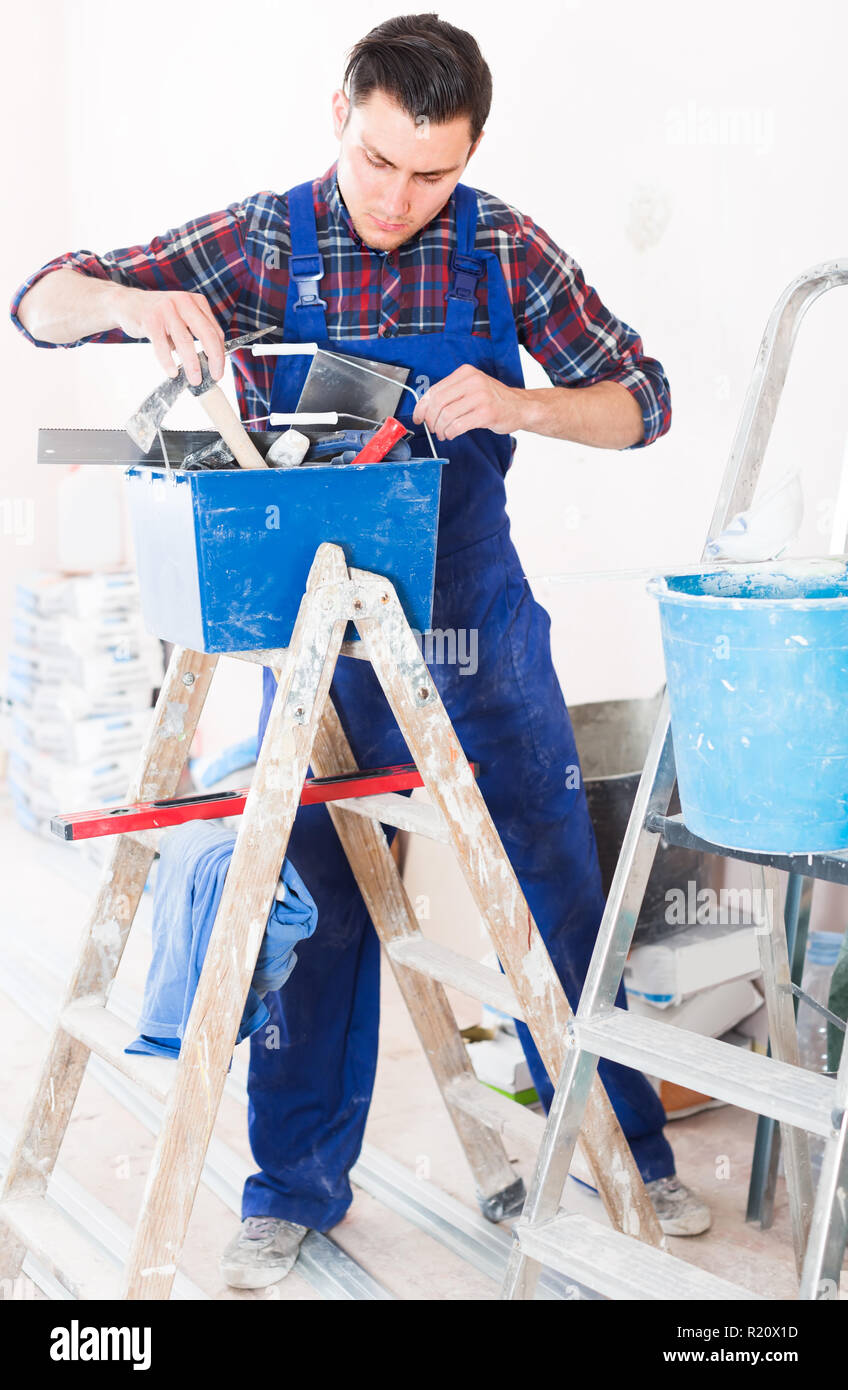 Young concentrated builder handyman choosing necessary tool in toolbox Stock Photo