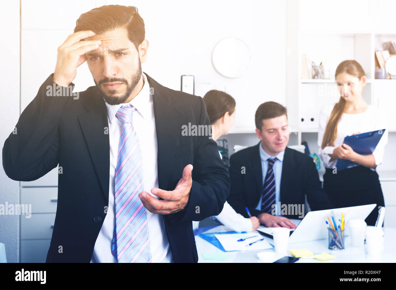 Business team tensely solving problems in office with upset man foreground Stock Photo