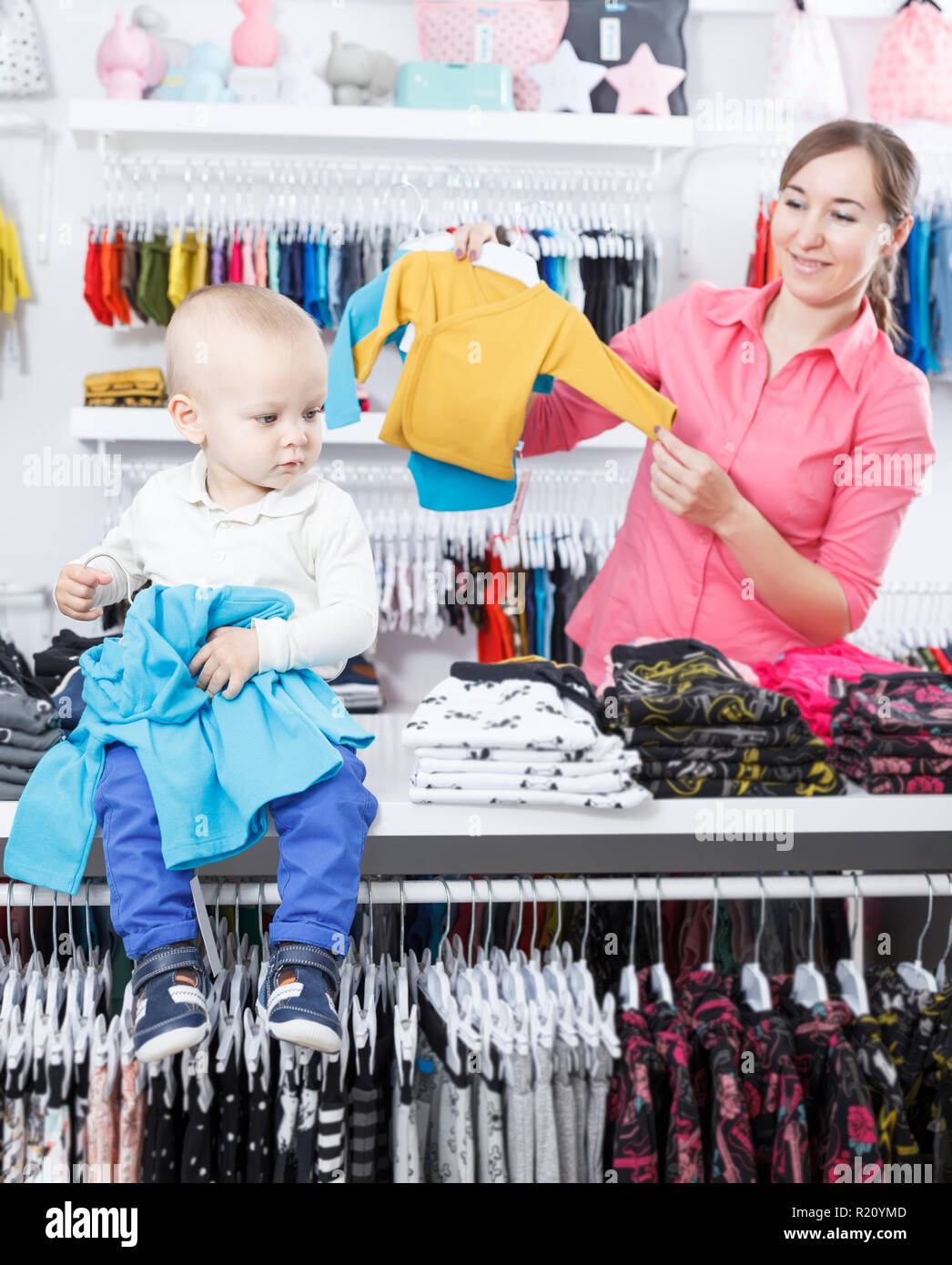 Smiling female with kid is choosing modern clothes for little son in ...
