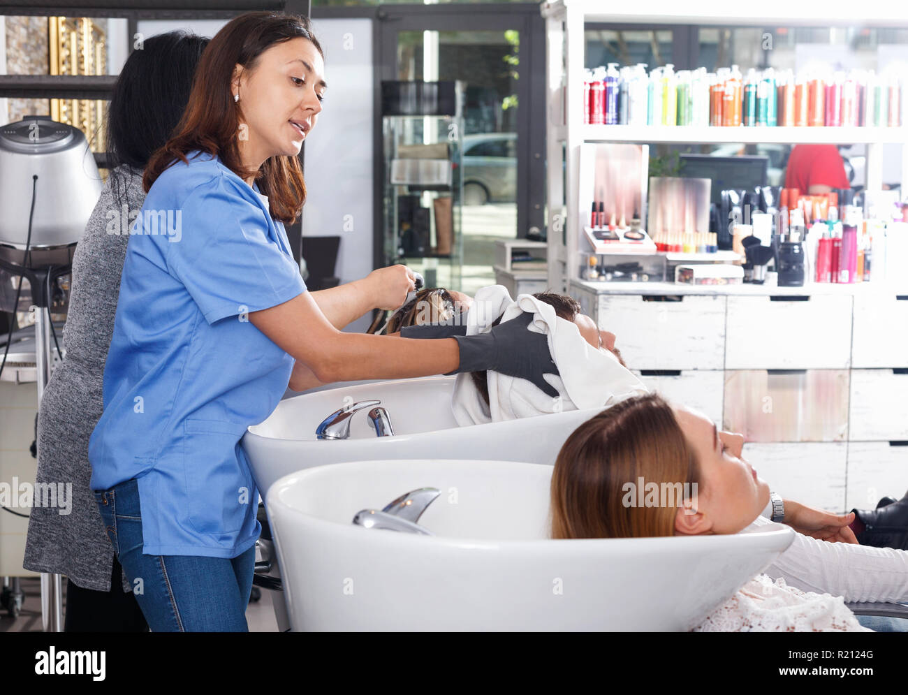 Portrait of glad positive woman hairdresser in gloves washing hair of