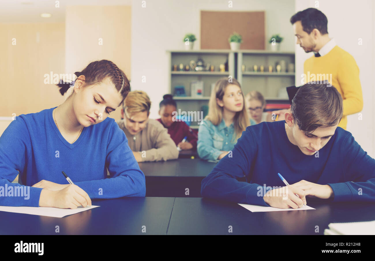 Serious positive teacher monitoring students’ work during examination test in class Stock Photo