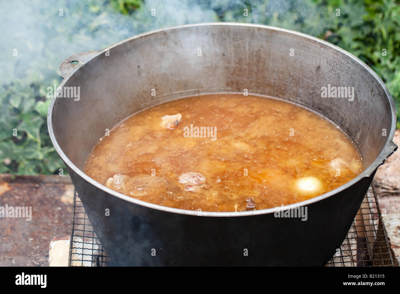 Broth with lamb and vegetables boil in a cauldron. Preparing of Chorba soup on open fire, traditional meal for many national cuisines in Europe, Afric Stock Photo