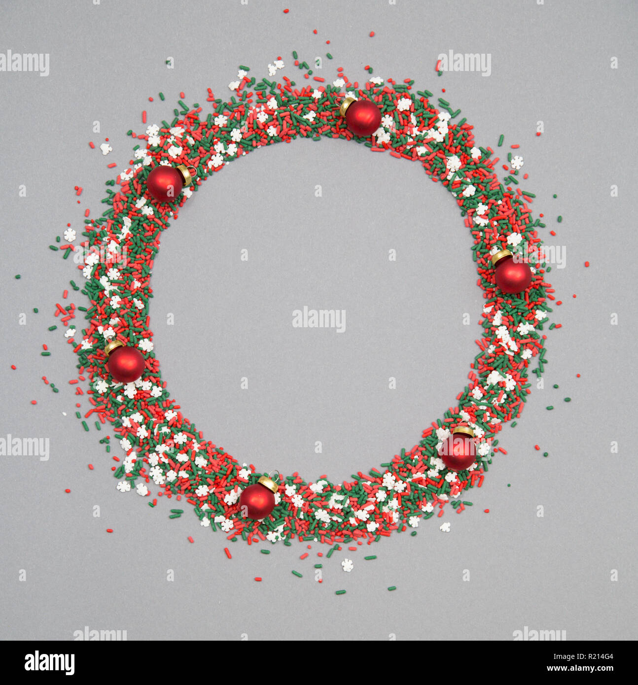 Christmas wreath made of red and green sprinkles with christmas ornaments on a grey background Stock Photo