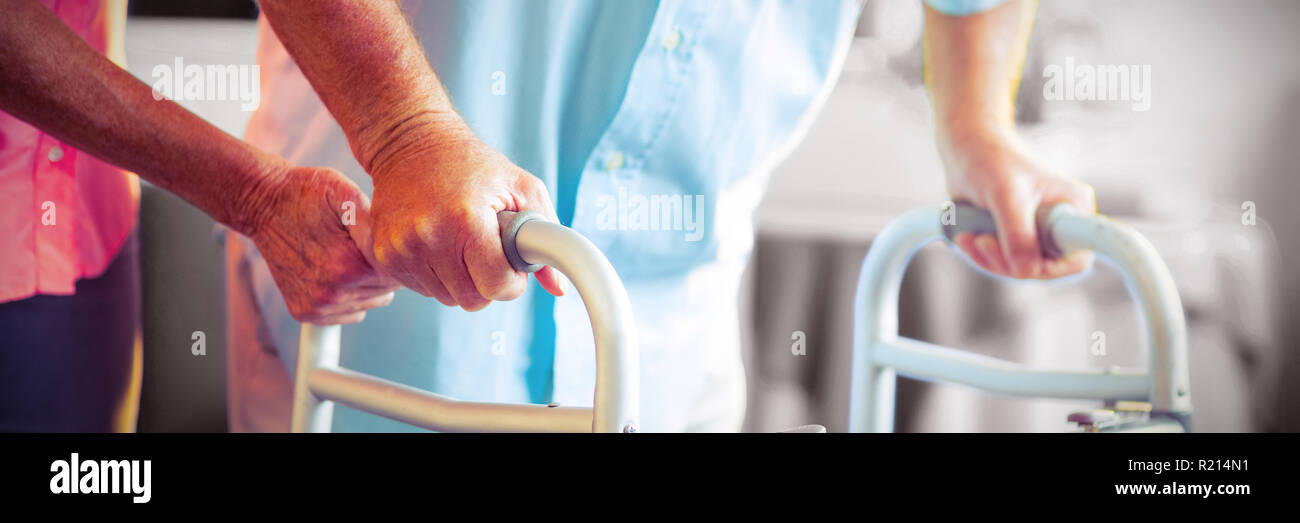 Senior woman helping senior man to walk with walker Stock Photo