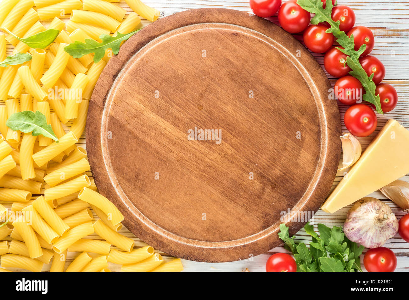 Italian Ingredients for cooking pasta with a kitchen board for copy space Cherry tomatoes arugula parmesan cheese rigatoni pasta garlic and olive oil. Concept food recipes top view flat lay Stock Photo