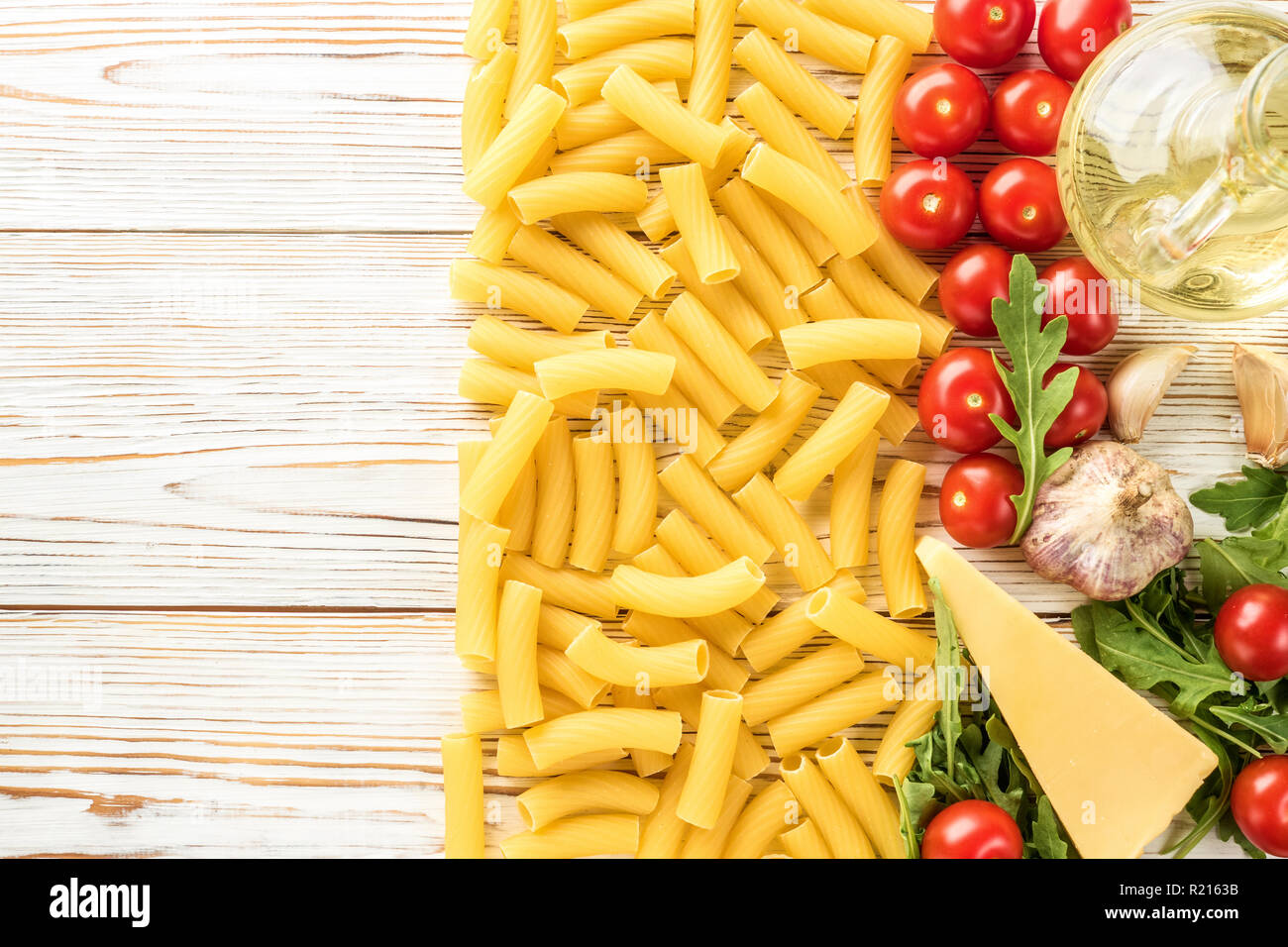 Italian Ingredients for cooking pasta with for copy space Cherry tomatoes arugula parmesan cheese rigatoni pasta garlic and olive oil. Concept food italian recipes top view flat lay Stock Photo