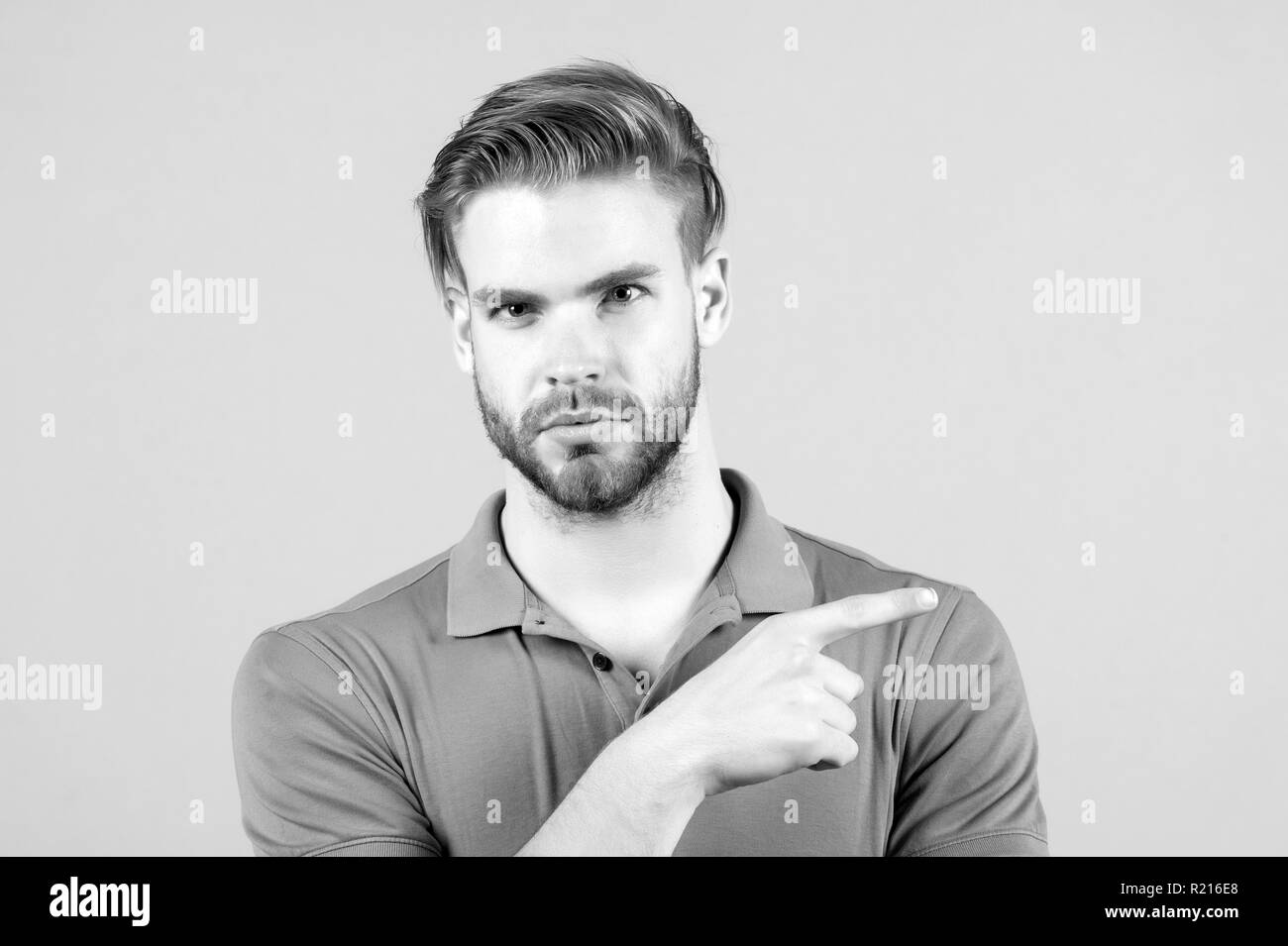he is perfect. Handsome young man in tshirt looking at camera and pointing away while standing against grey background. Stock Photo