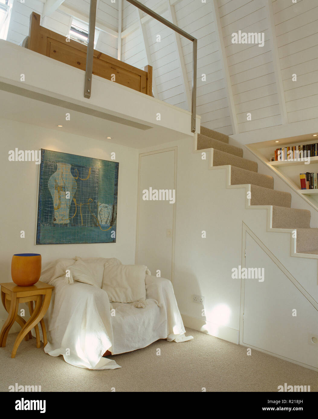 White throw on armchair beside staircase in modern hall Stock Photo
