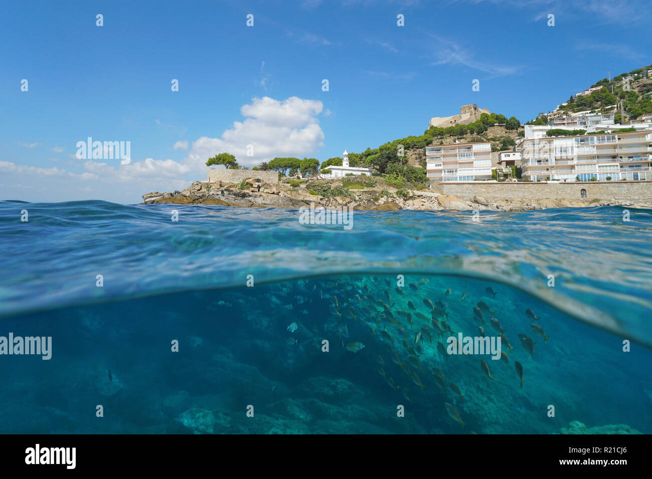 A lighthouse and buildings on a rocky coastline with a school of fish underwater, split view, Spain, Costa Brava, Roses, Mediterranean sea, Catalonia Stock Photo