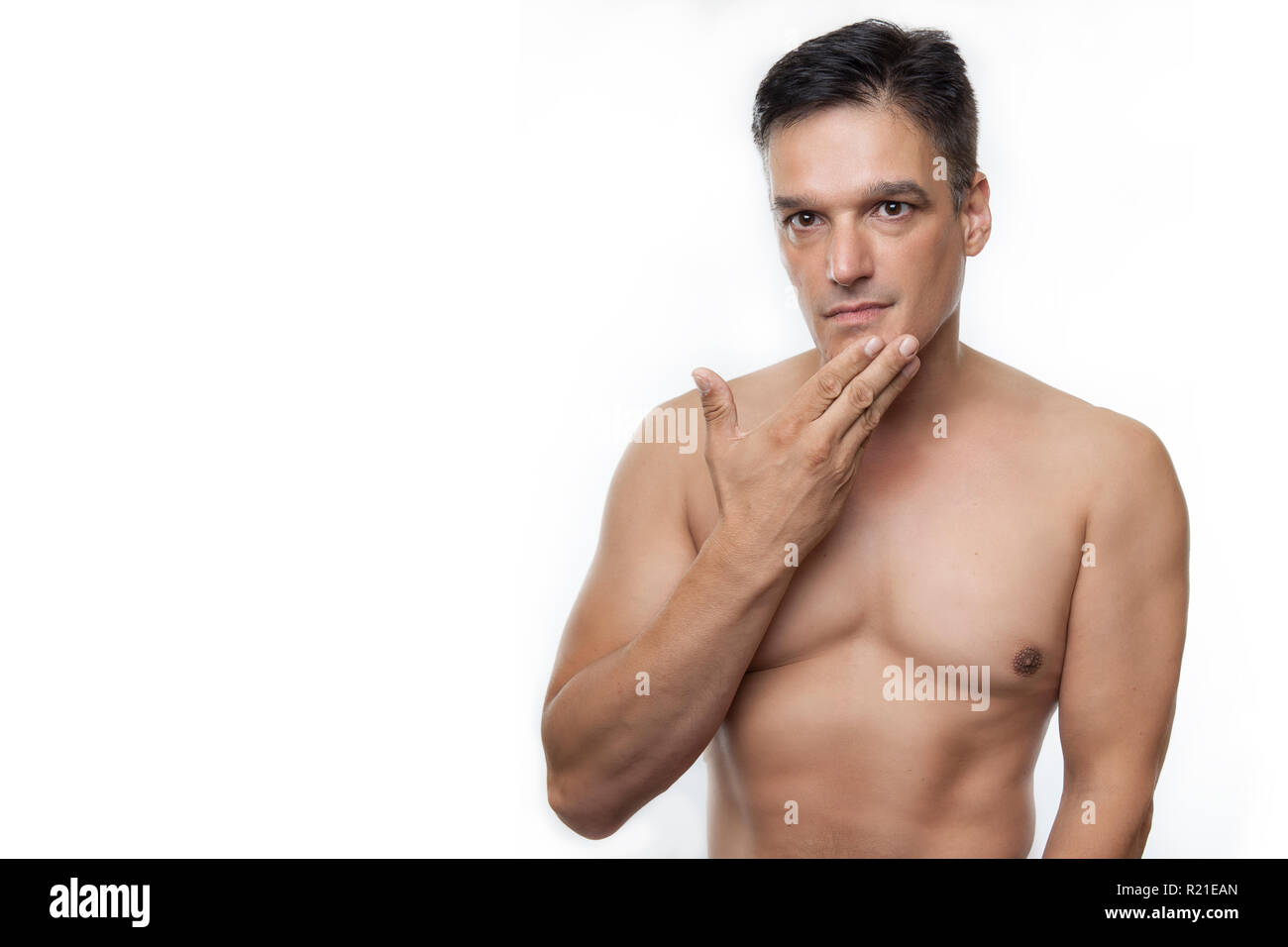 Shirtless young man with hand to chin against white background. Studio shot Stock Photo