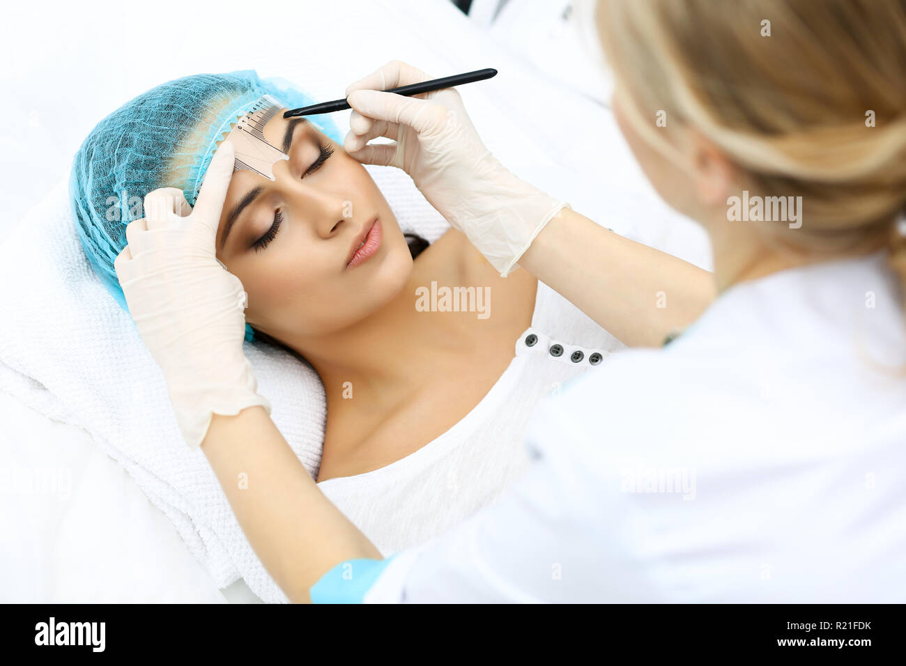 Professional beautician is going to correct eyebrow line at woman face ...