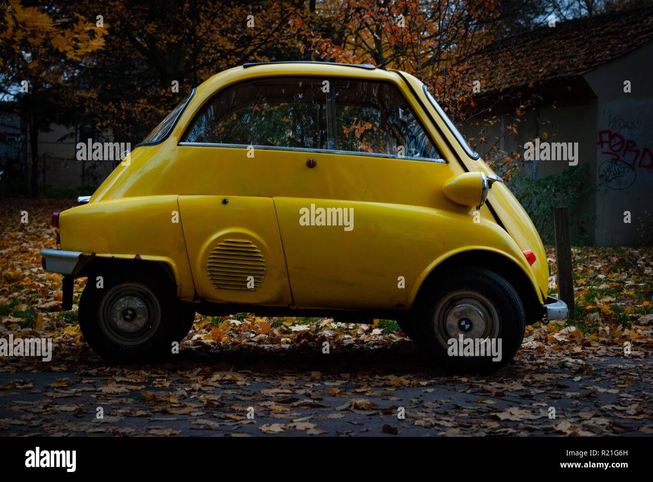 A tiny yellow old car car in autumn Stock Photo