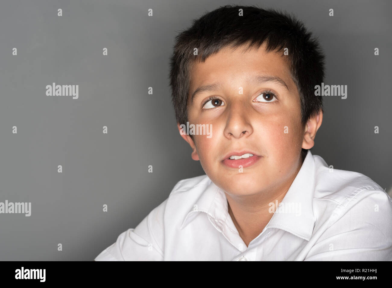 UK, head and shoulders portrait of a young schoolboy in school uniform on grey background Stock Photo