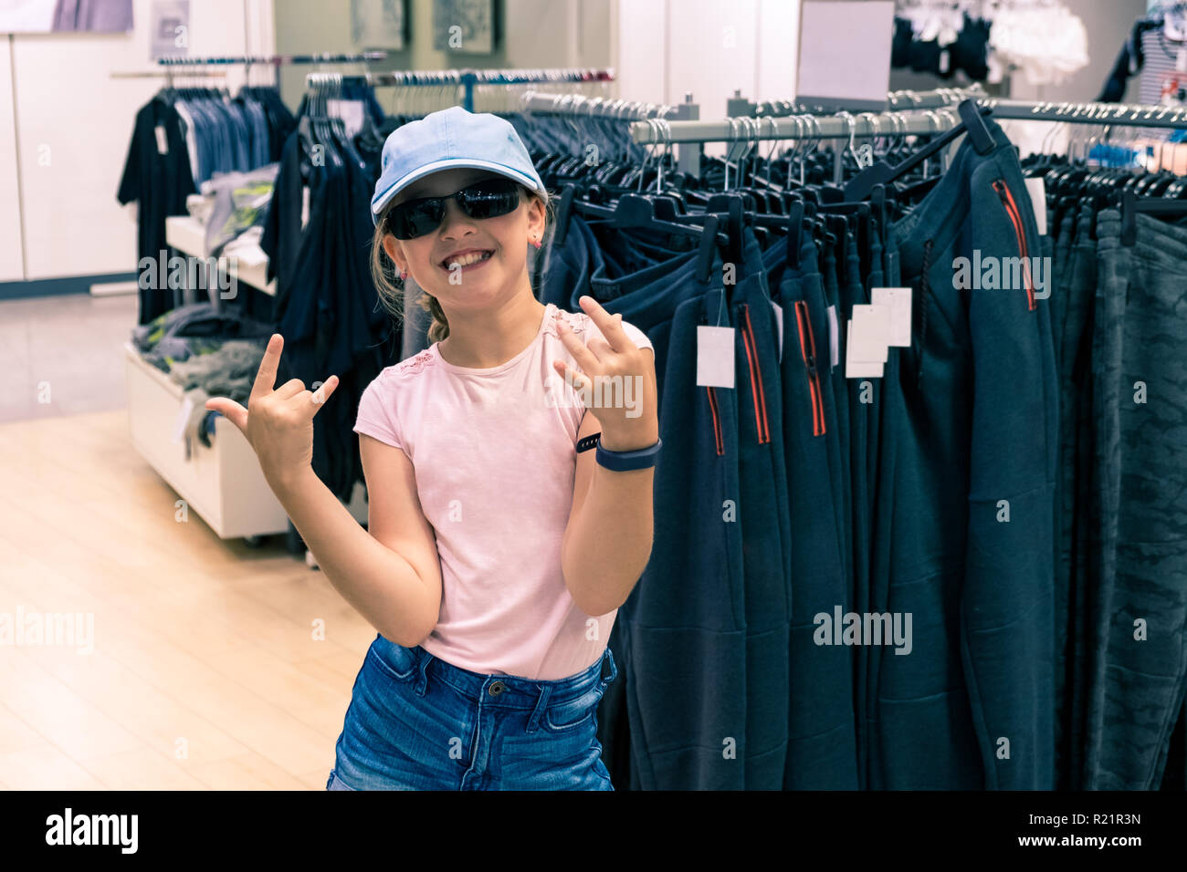 Portrait of young trendy girl with pink t-shirt, sunglasses and baseball cap in department store Stock Photo