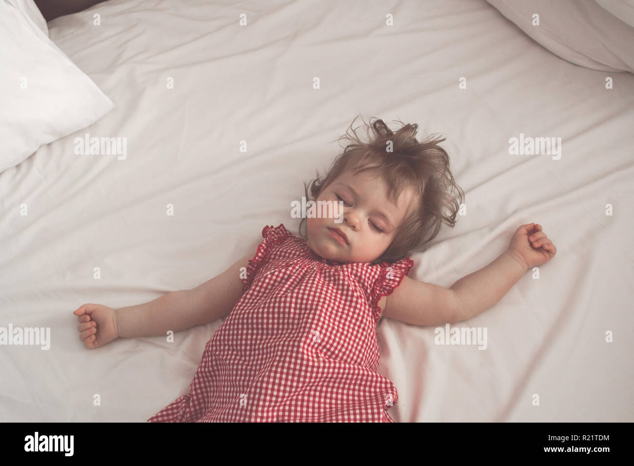Baby girl sleeping on back with open arms and without pacifier in a bed