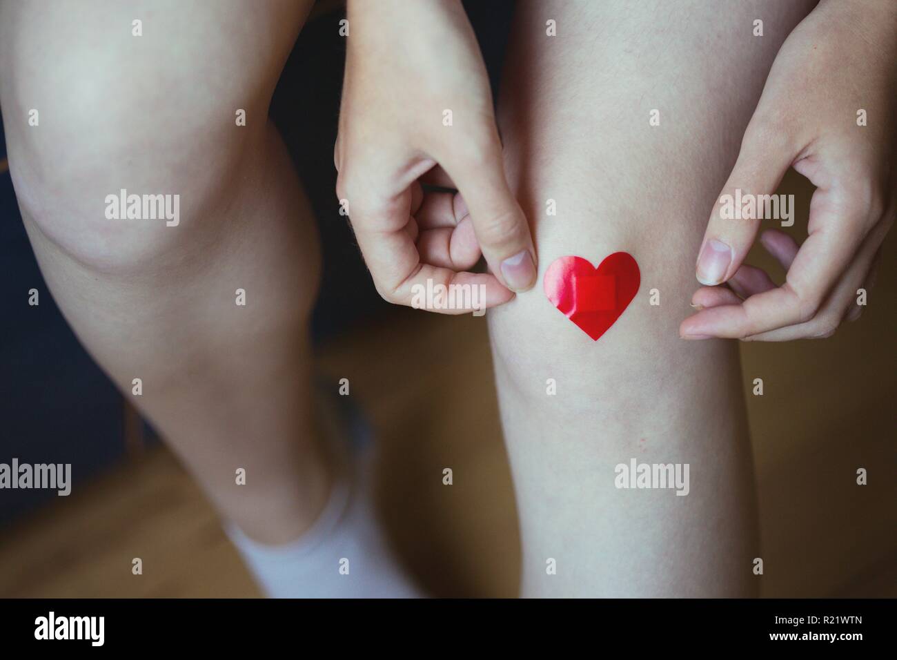 girl glues medical plaster in the form of a red heart on the leg Stock Photo
