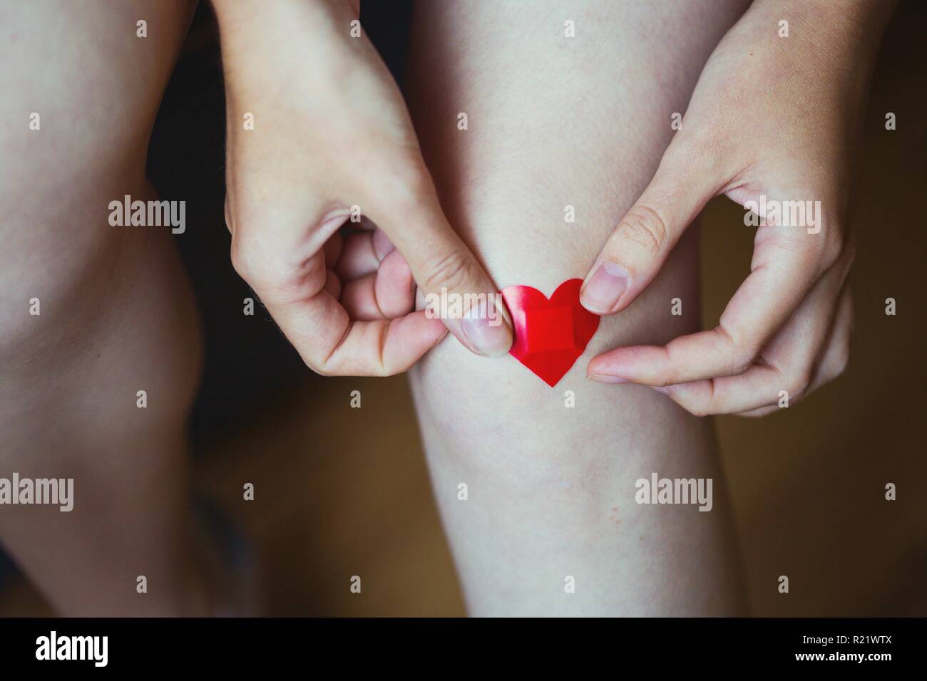 girl glues medical plaster in the form of a red heart on the leg Stock Photo