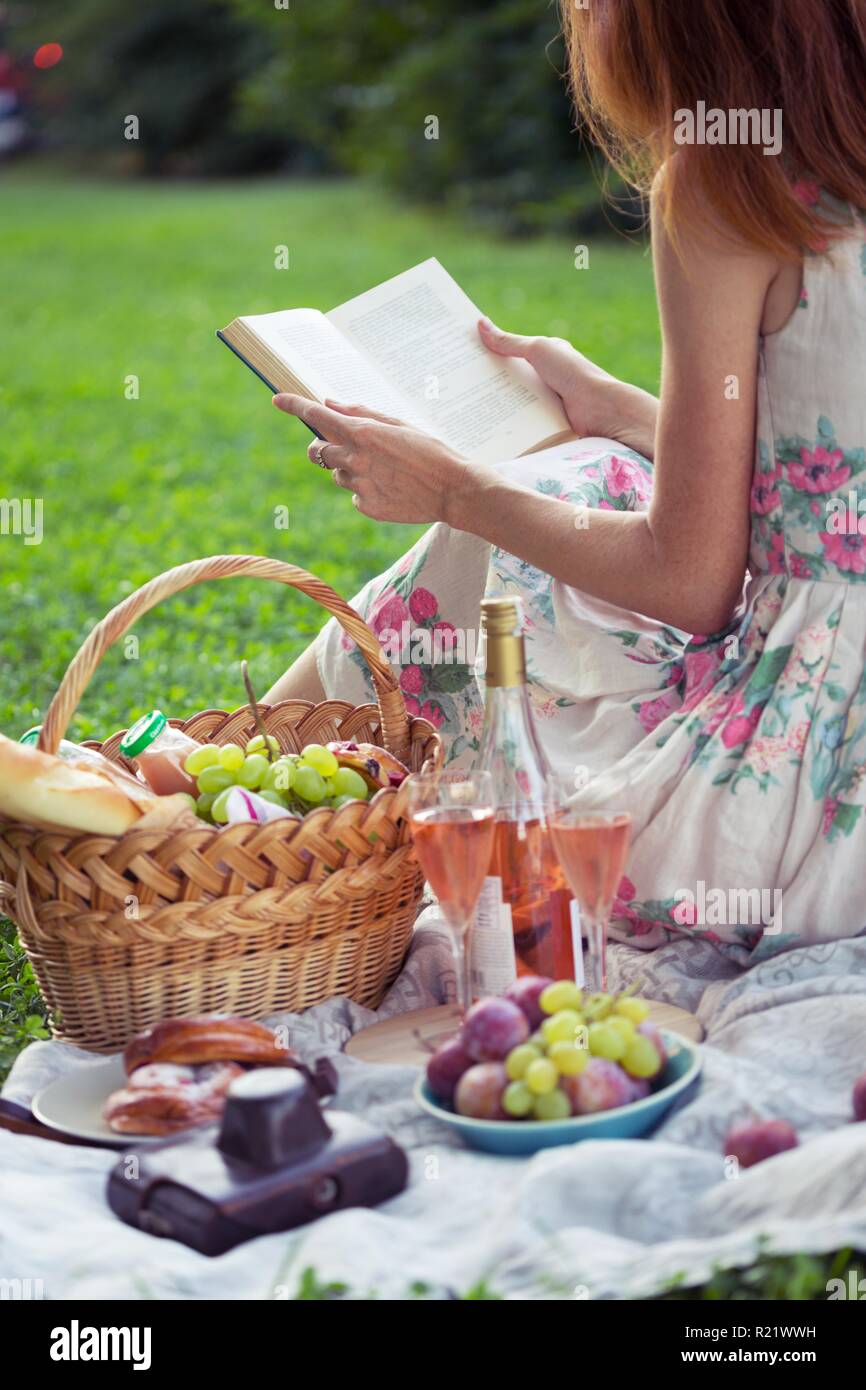 Summer - picnic in the meadow. girl sitting reading a book and near a picnic  basket and baguette, wine, glasses, grapes and rolls Stock Photo - Alamy