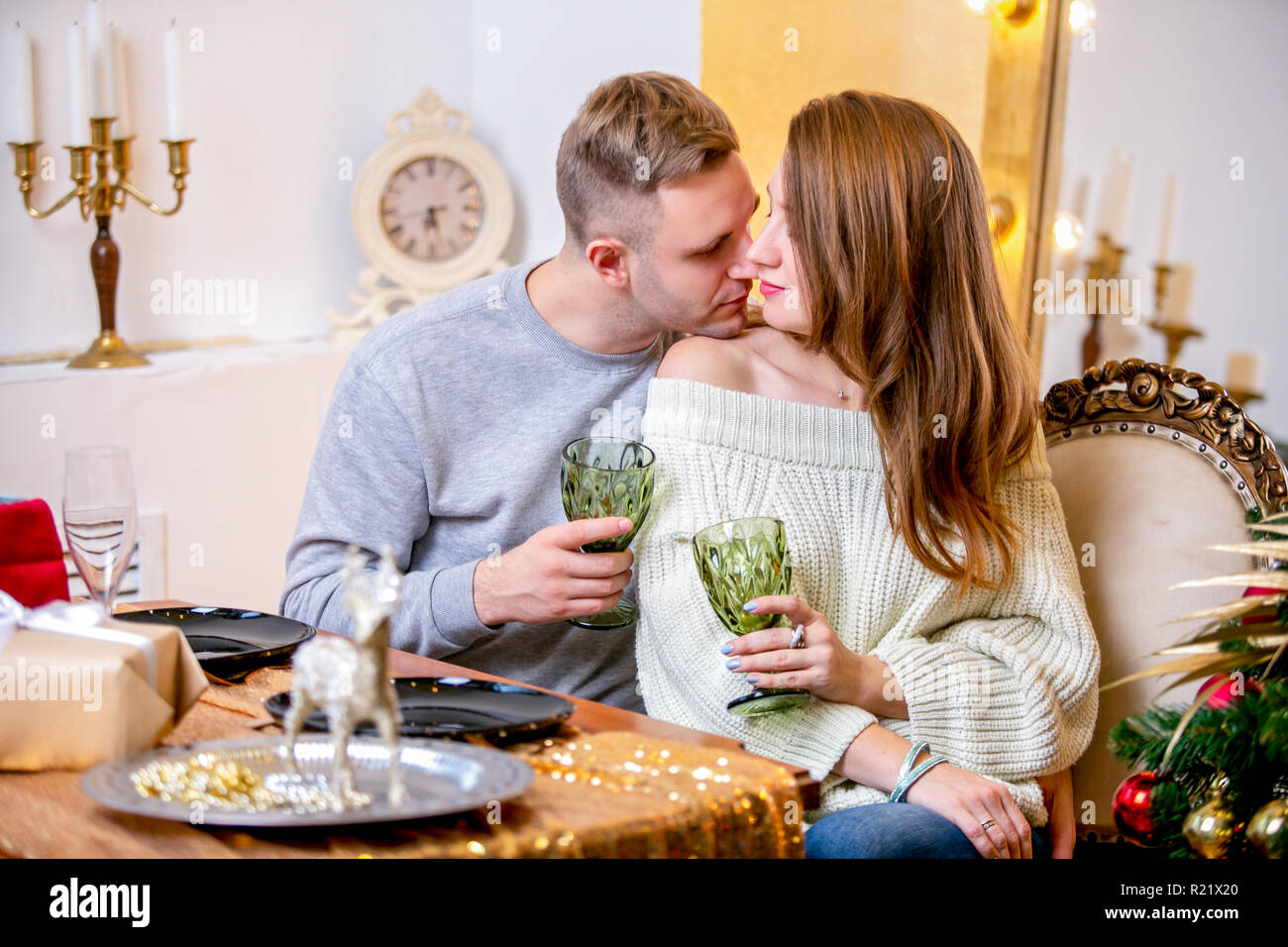 Happy young family in Christmas evening in home. They sitting at the table at Christmas dinner. They hugging and kissing. Romantic mood. New Year's an Stock Photo