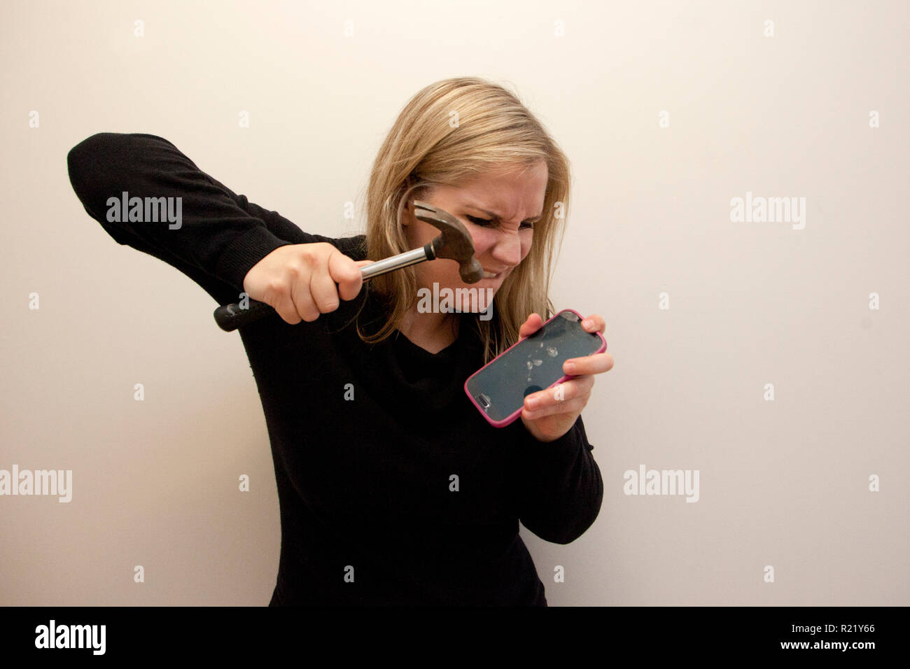 An angry woman takes a hammer and smashes her cell phone Stock Photo