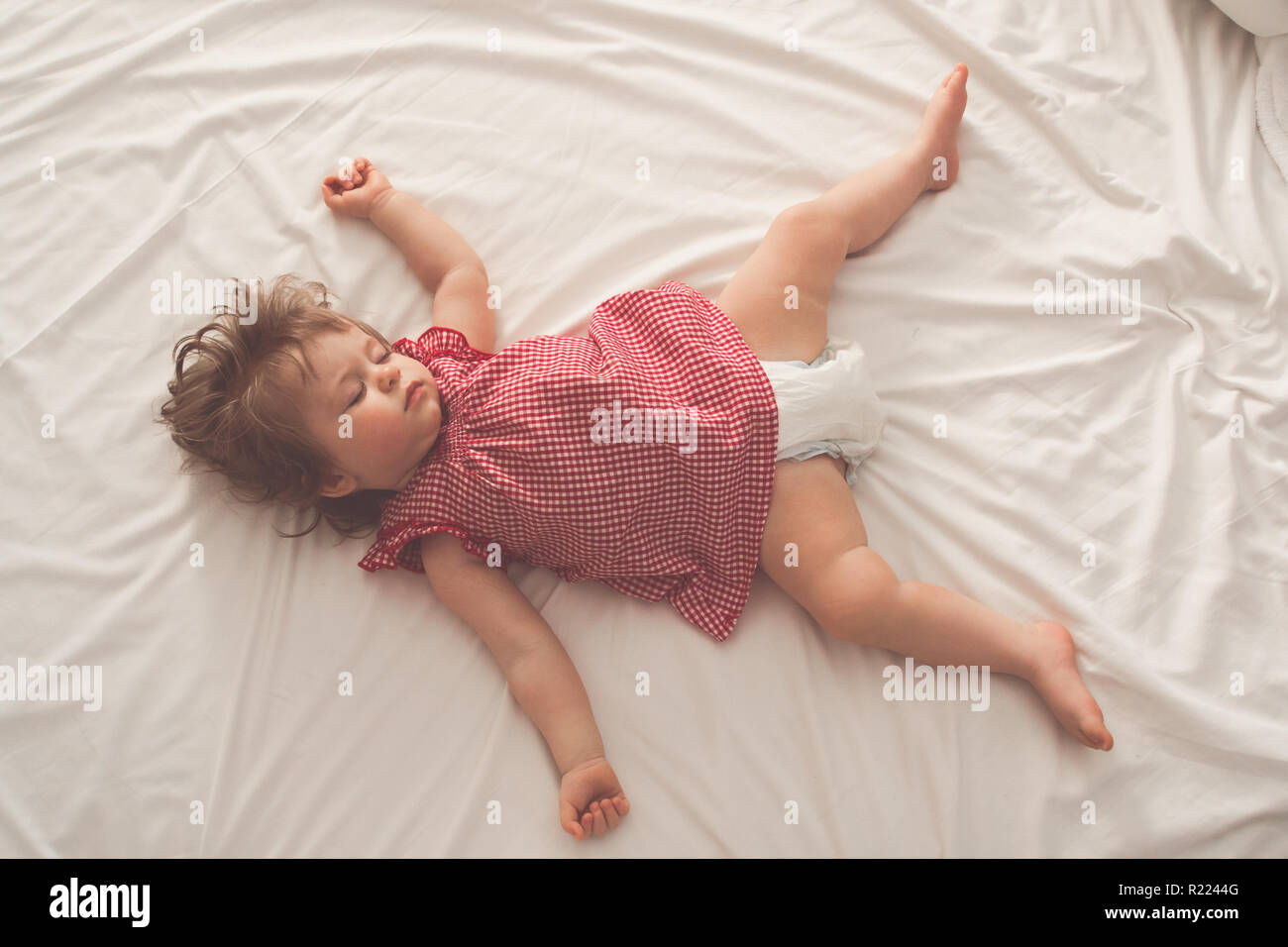 Baby girl sleeping on back with open arms and without pacifier in a bed