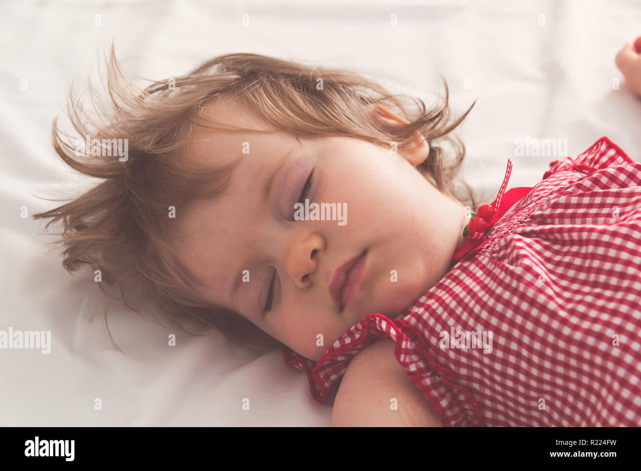 Baby girl sleeping on back with open arms and without pacifier in a bed with white sheets. Peaceful sleeping in a bright room. Pastel retro toned. Sof Stock Photo