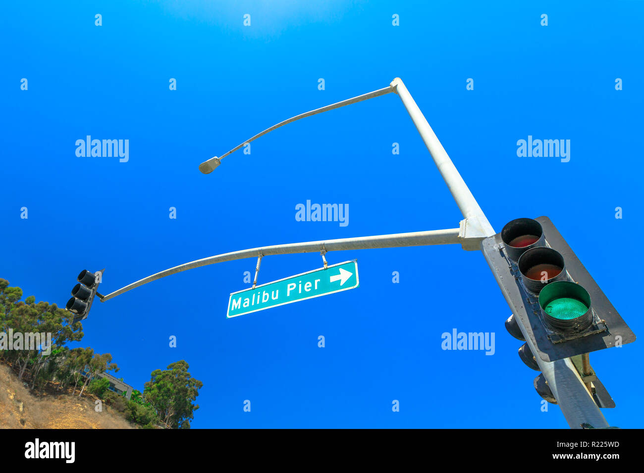 Bottom view of green Traffic Light and Malibu Pier Sign in the sunny day with blue sky. Malibu Pier is a historic landmark in California, on the Pacific Coast Highway, United States. Copy space. Stock Photo