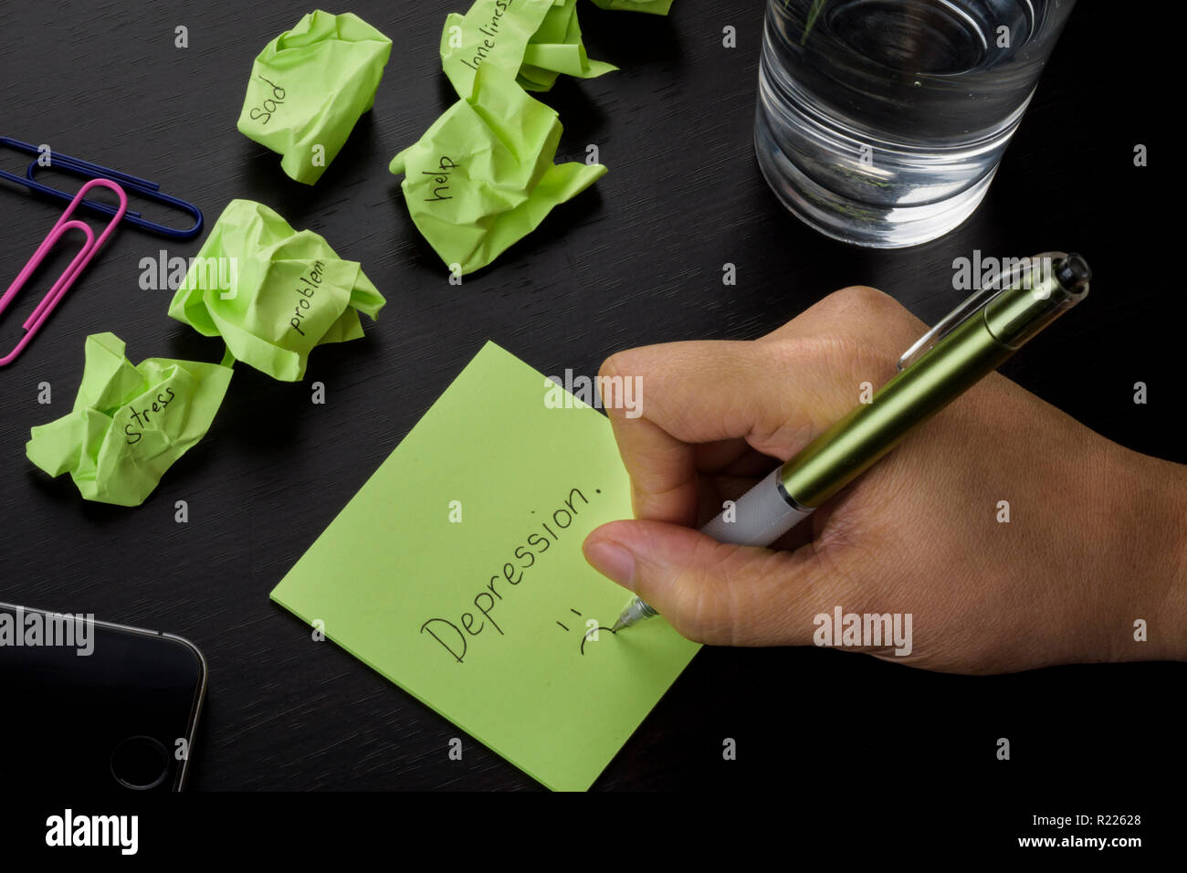A hand writing on a green sticky note the word 'depression.' A photo about depression, sadness and loneliness. Crumpled green sticky notes scattered. Stock Photo