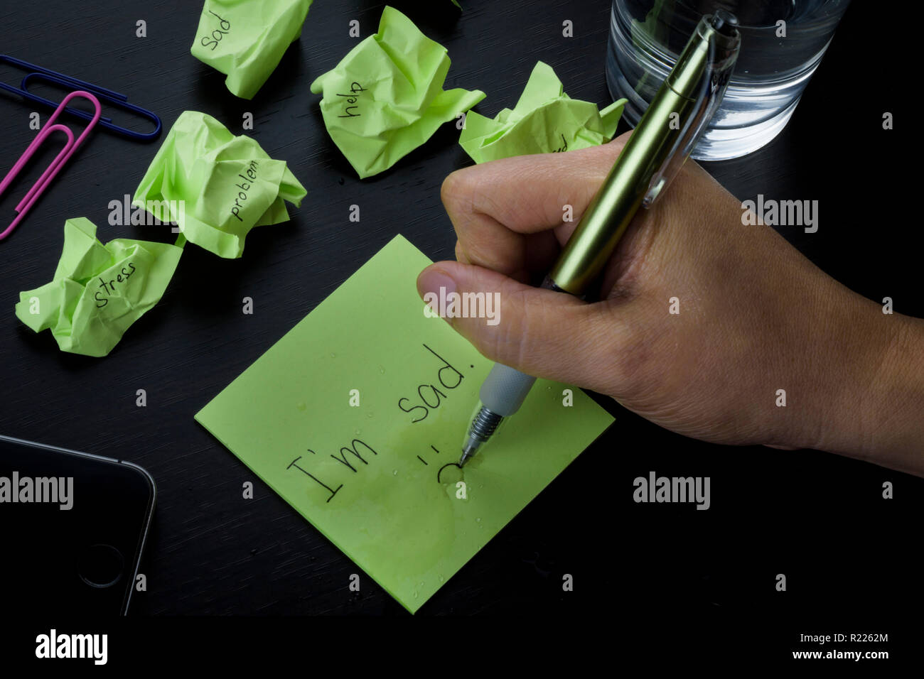A hand writing on a green sticky note the phrase 'I'm sad.' A photo about depression, sadness and loneliness. Crumpled green sticky notes scattered. Stock Photo
