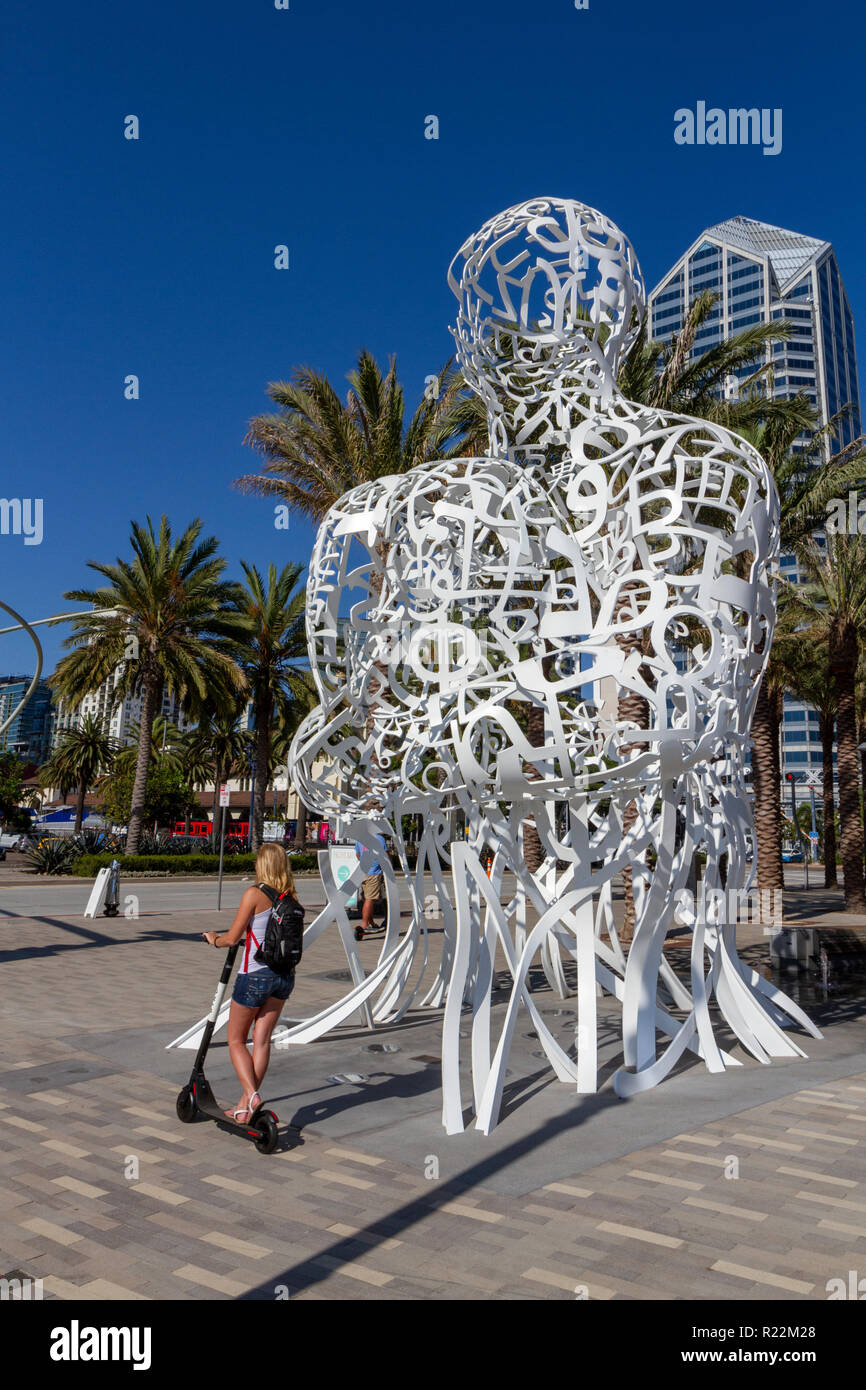 Woman on electric scooter passing 'Pacific Soul' by Jaume Plensa, on the corner of Pacific Highway and Broadway in San Diego, California, USA. Stock Photo