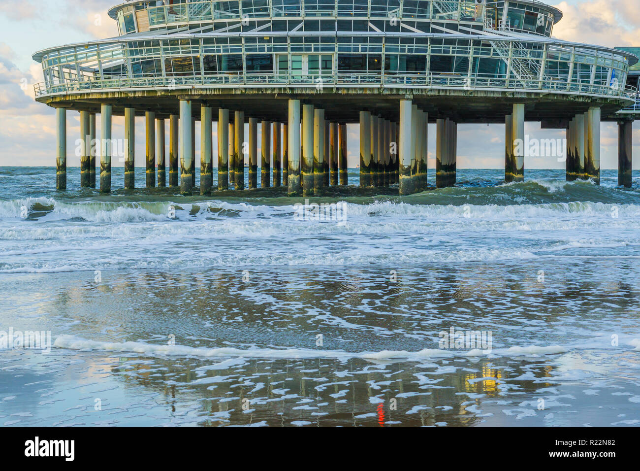 building on stone weathered poles at the beach of scheveningen with waves in the sea and reflection in the wet sand Stock Photo