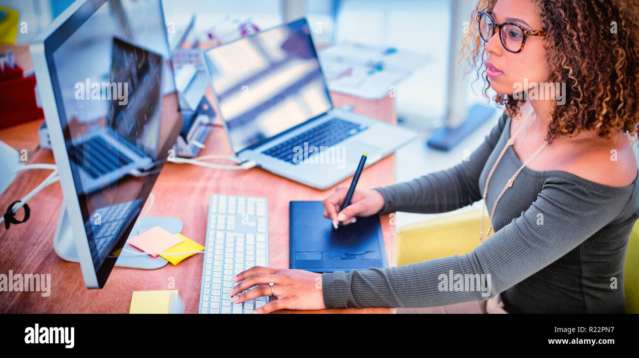 Female graphic designer working on computer while using graphic tablet at desk Stock Photo