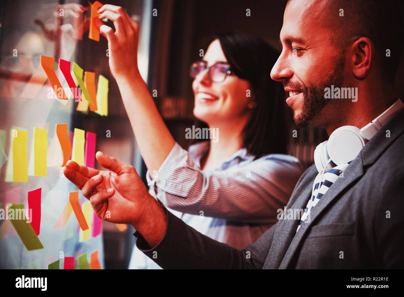 Coworkers sticking adhesive notes on glass Stock Photo