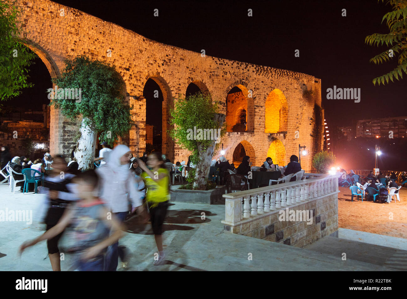 Hama, Hama Governorate, Syria : Syrian families sit at night at the open-air coffeehouse by the old aqueduct which used to supply the Grand Mosque wit Stock Photo