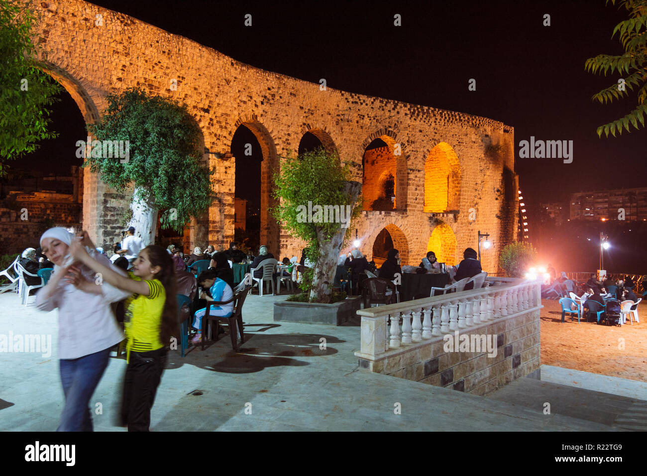 Hama, Hama Governorate, Syria : Syrian families sit at night at the open-air coffeehouse by the old aqueduct which used to supply the Grand Mosque wit Stock Photo