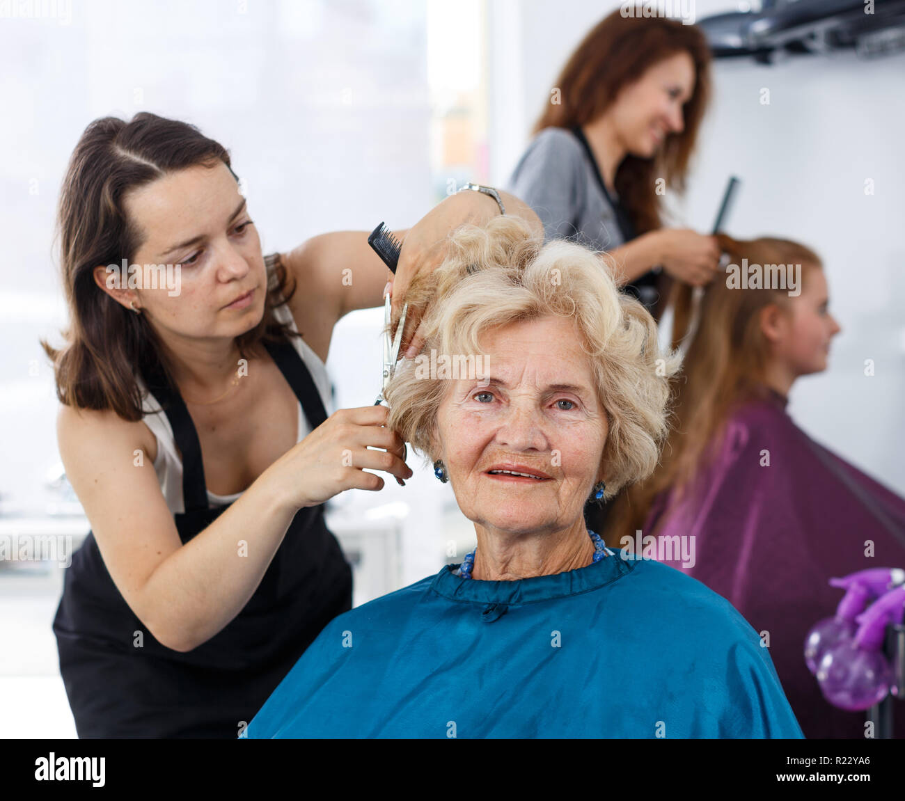 Skilled Woman Hairdresser Making Hairstyle For Elderly Female