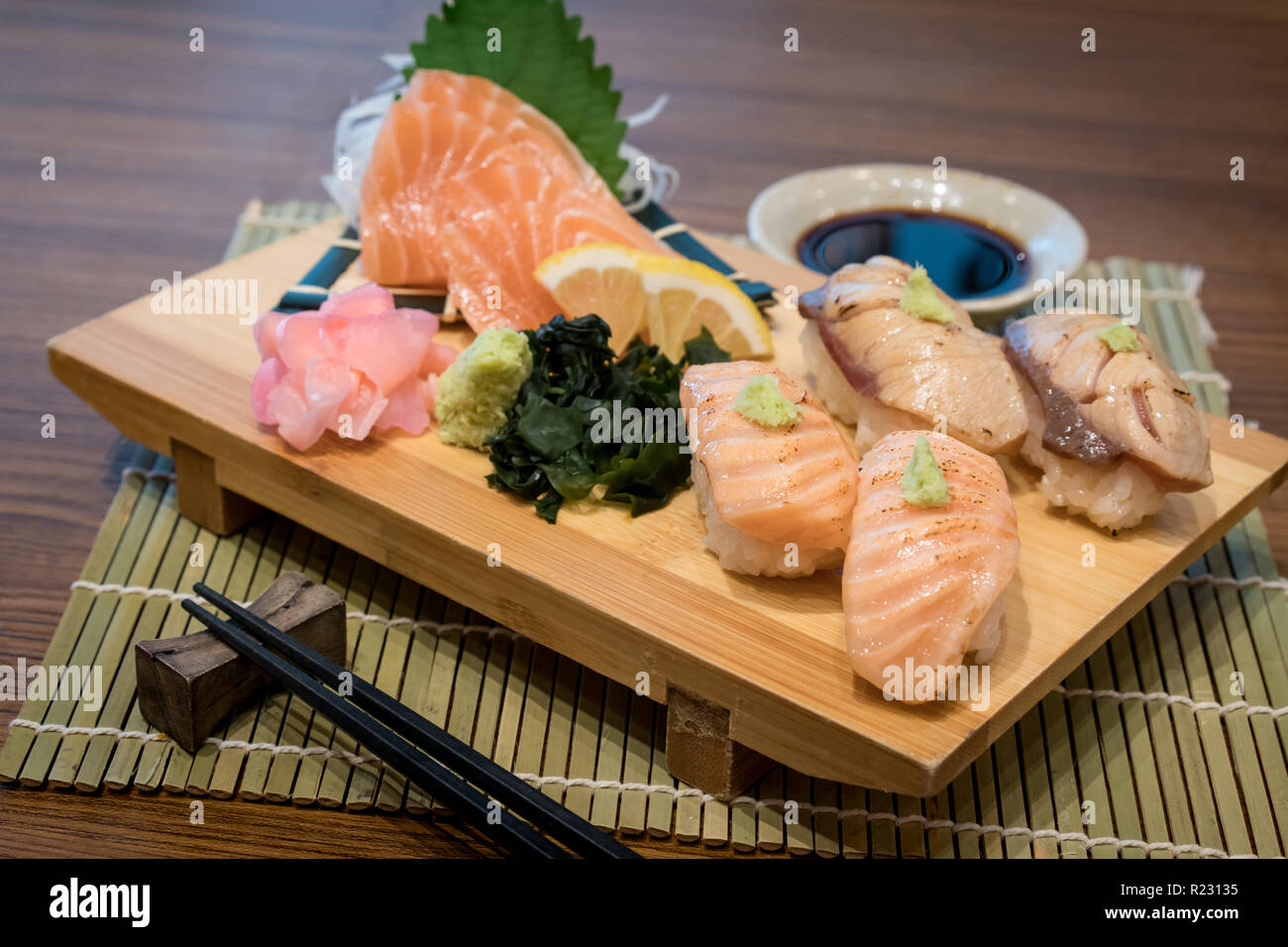 Mixed salmon sushi on wooden plate along with Japanese sauce and green leaf decoration, Japanese food, close up at sushi . Stock Photo