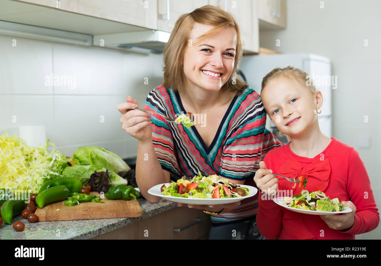 Happy mother and daughter eating vegetable salad in kitchen Stock Photo