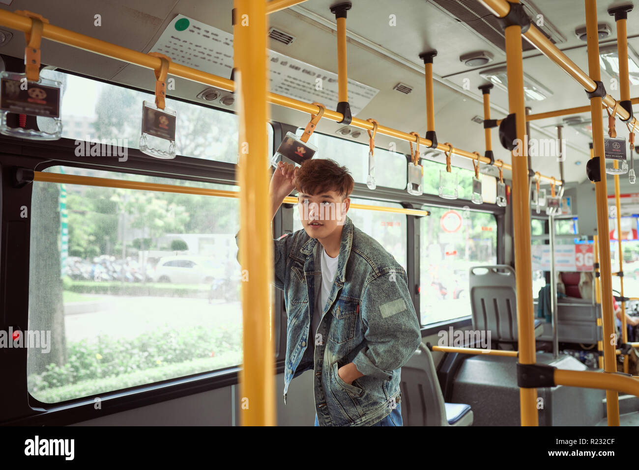 Young cheerful handsome man is holding onto the bar while standing in a bus. Stock Photo