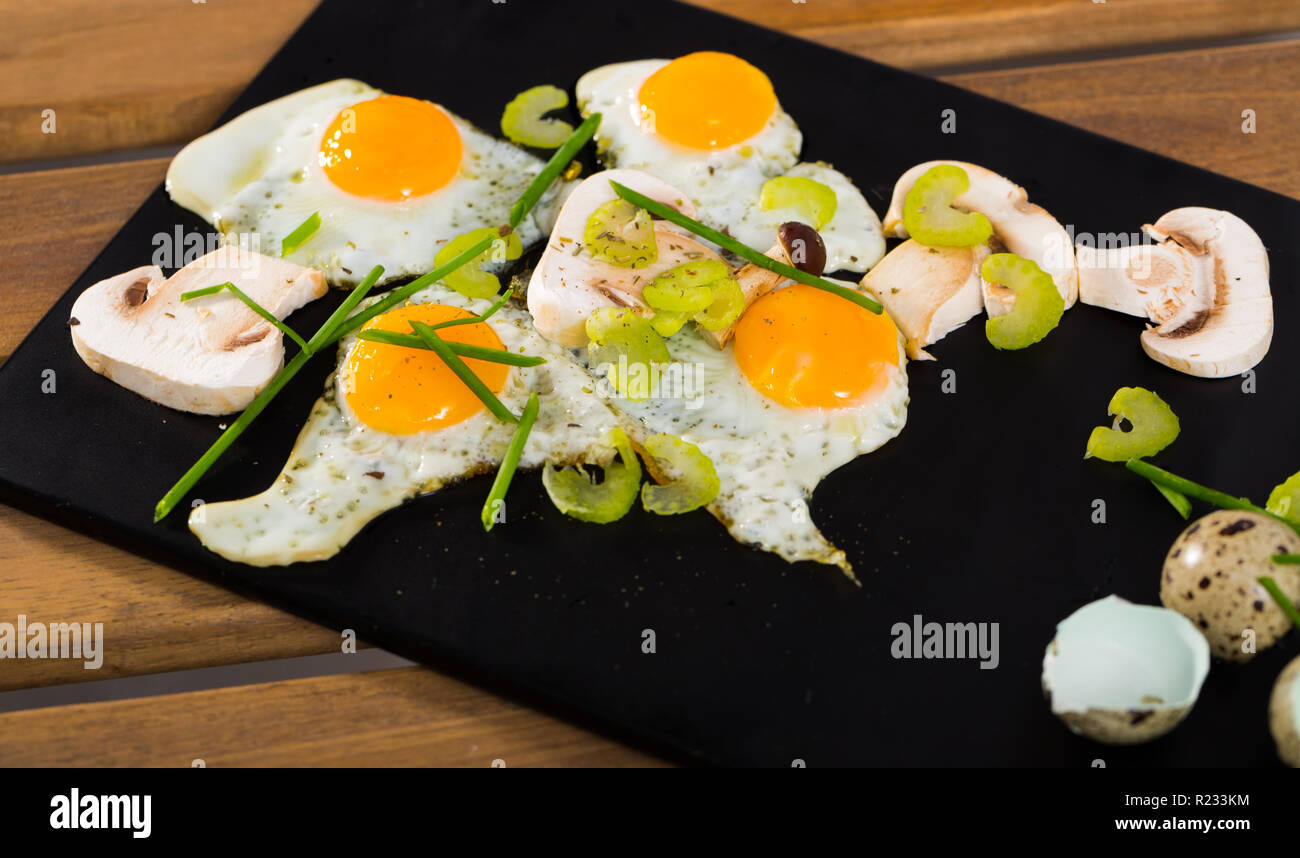 Fried quail eggs with mushrooms, chives and celery on wooden table Stock Photo