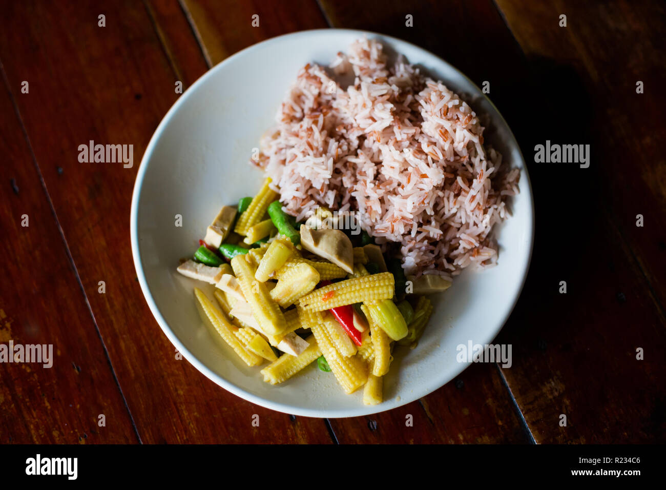 Fresh prepared asian spicy tofu baby corn thai stirfry served with red jasmine rice. Traditional thai cuisine made of fresh ingredients. Stock Photo