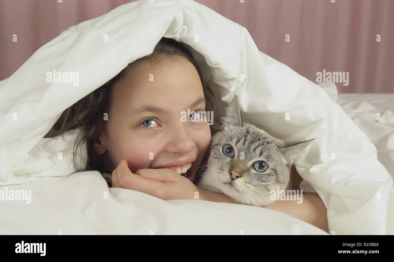Happy teen girl kisses and talks with Thai cat in bed Stock Photo